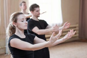 Drei Personen in schwarzer Kleidung üben in einem Amema-Studio Tanzbewegungen mit konzentrierter Mimik.